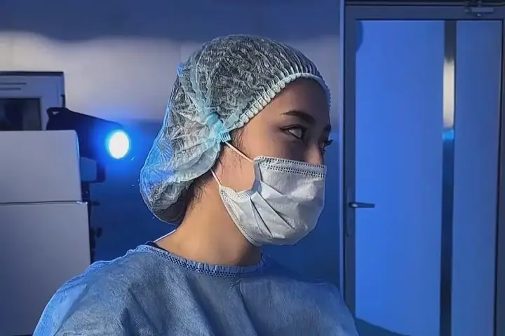 Операционная сестра в шапочке и маске у лазера перед лазерной коррекцией зрения