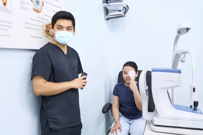Девочка закрывает один глаз окклюдером, врач BABY EYE CLINIC проверяет остроту зрения второго
