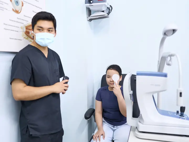 Девочка закрывает один глаз окклюдером, врач BABY EYE CLINIC проверяет второй