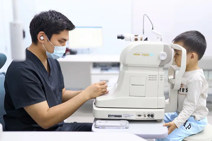 Врач BABY EYE CLINIC измеряет зрение мальчику на приборе